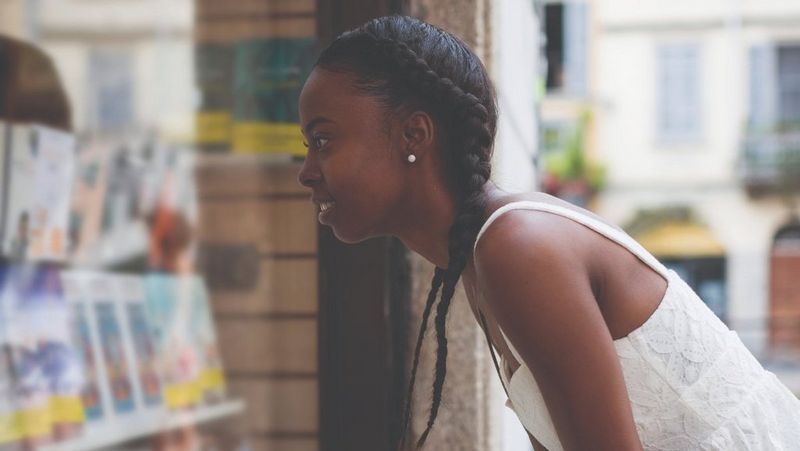 A woman looking through a shop window at a rack of books